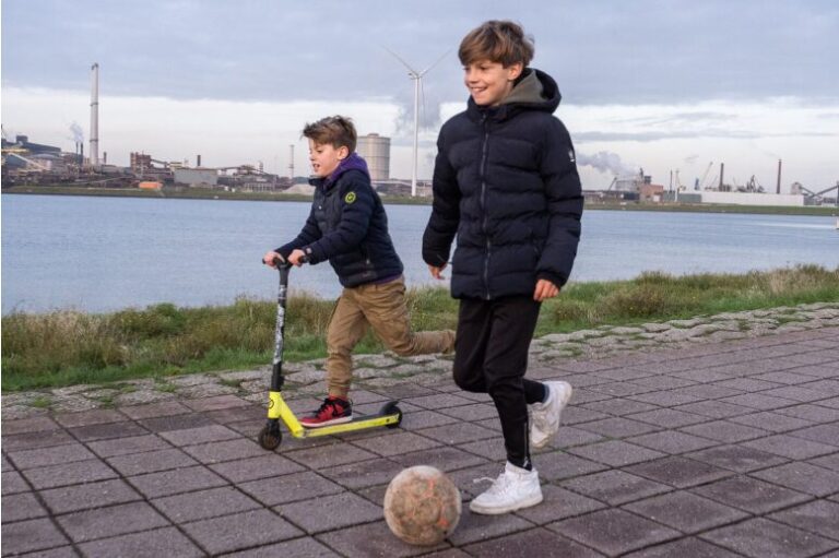 Spelende kinderen aan de waterkant met op de achtergrond industrie
