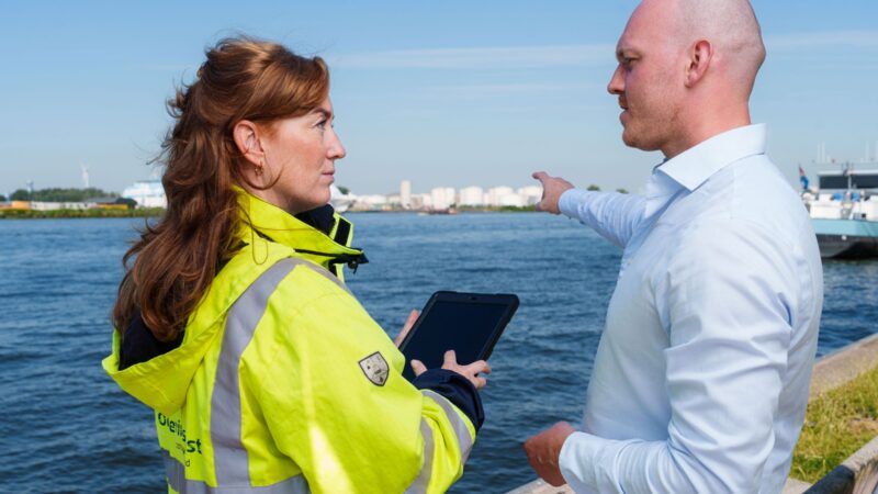 Vergunningverlener en toezichthouder aan de waterkant wijzend naar vloeistofopslag